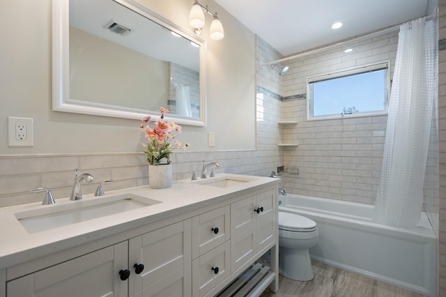 full bathroom featuring hardwood / wood-style floors, tile walls, vanity, shower / tub combo, and toilet