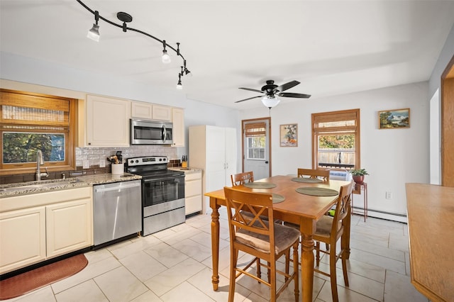 kitchen featuring sink, baseboard heating, stainless steel appliances, light stone countertops, and backsplash