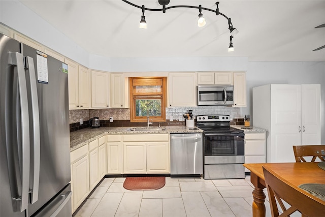 kitchen featuring sink, dark stone countertops, appliances with stainless steel finishes, decorative backsplash, and cream cabinetry