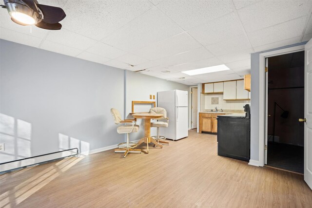 kitchen featuring sink, a paneled ceiling, baseboard heating, white refrigerator, and light hardwood / wood-style floors