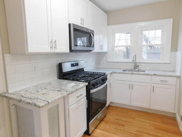 kitchen with stainless steel appliances, sink, white cabinets, and light hardwood / wood-style floors