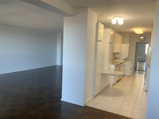 kitchen with sink, white cabinets, white refrigerator, light tile patterned floors, and a textured ceiling