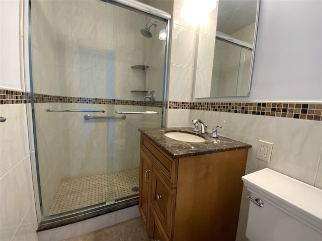 bathroom with vanity, toilet, a shower with shower door, and tile walls