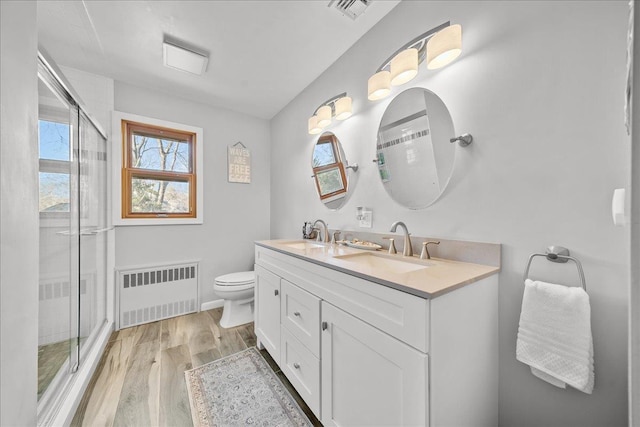 bathroom featuring radiator heating unit, a shower with door, hardwood / wood-style floors, and vanity