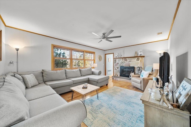 living room featuring hardwood / wood-style flooring, a stone fireplace, ornamental molding, and ceiling fan