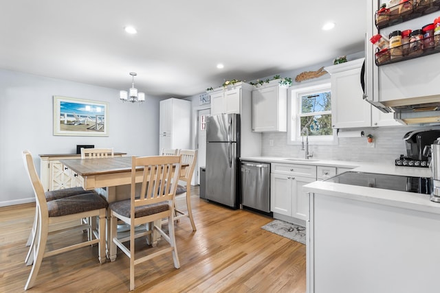 kitchen with decorative light fixtures, sink, white cabinets, stainless steel appliances, and light hardwood / wood-style flooring