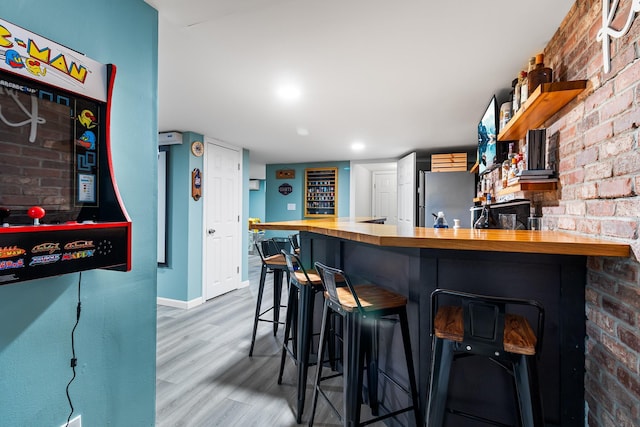 bar featuring butcher block countertops, wood-type flooring, stainless steel refrigerator, and brick wall