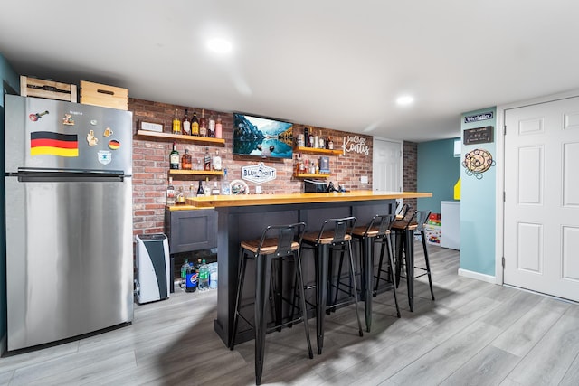 bar with brick wall, stainless steel fridge, wood counters, and light hardwood / wood-style flooring