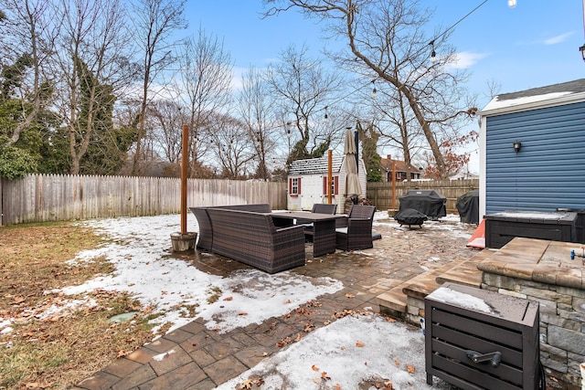 snow covered patio featuring a grill and a storage shed