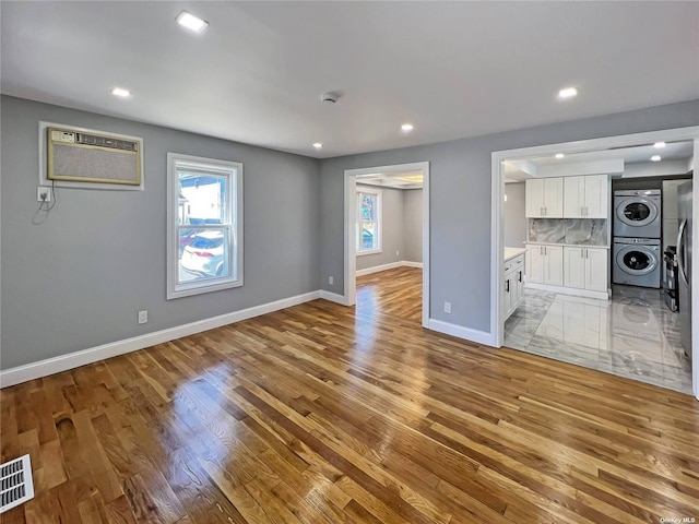 unfurnished living room featuring stacked washing maching and dryer, light hardwood / wood-style floors, and a wall unit AC