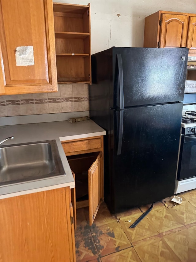 kitchen featuring sink, black refrigerator, tasteful backsplash, gas range oven, and parquet floors