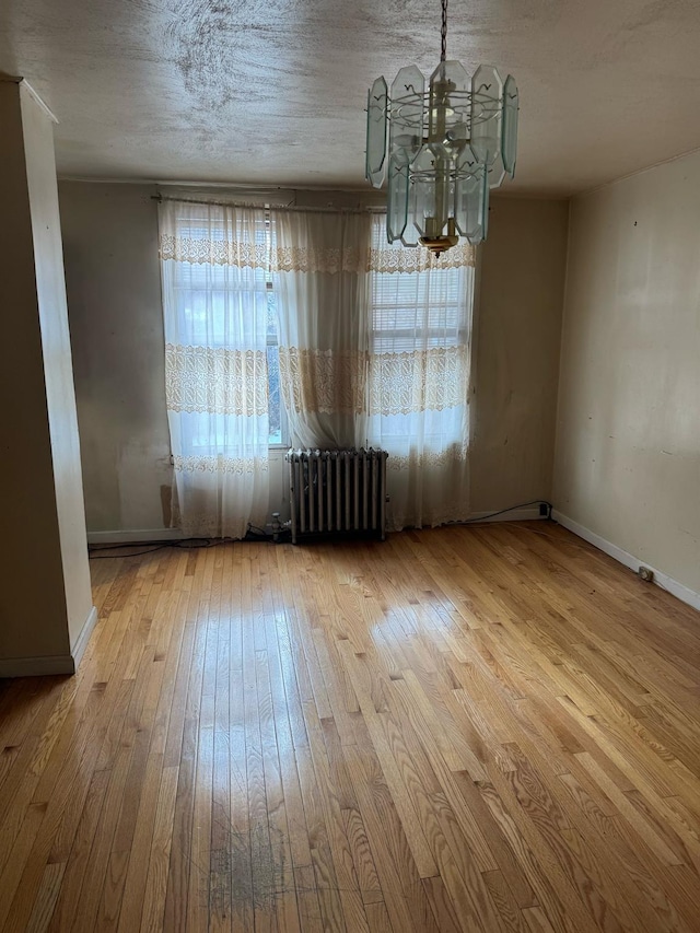 unfurnished dining area with wood-type flooring, radiator heating unit, a notable chandelier, and a textured ceiling