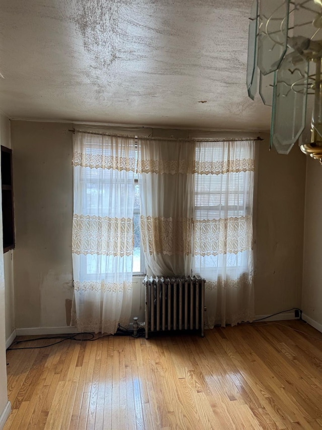 unfurnished room with a wealth of natural light, radiator heating unit, a textured ceiling, and light hardwood / wood-style flooring