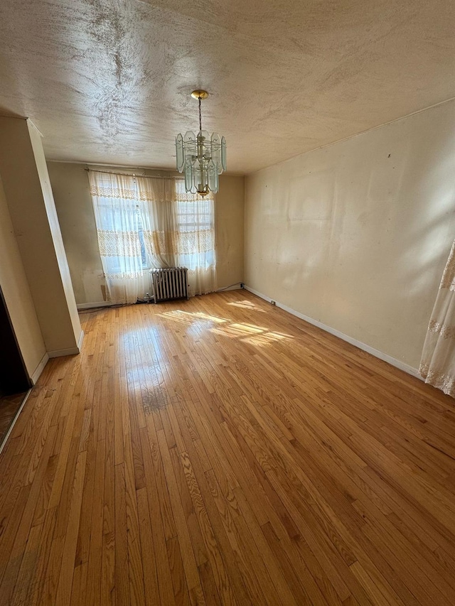 unfurnished dining area featuring a notable chandelier, hardwood / wood-style flooring, radiator heating unit, and a textured ceiling