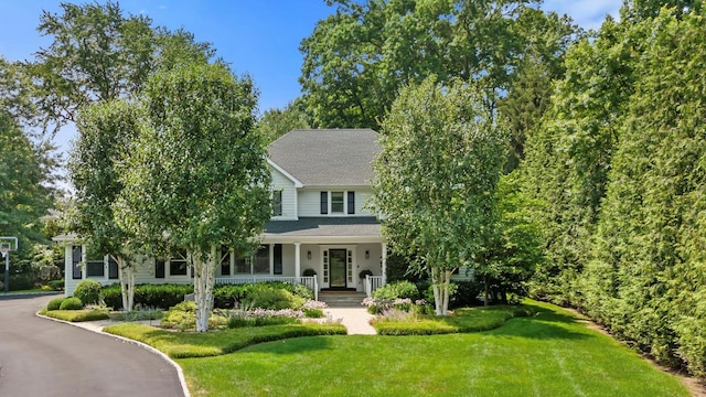 view of front facade featuring driveway, covered porch, a front lawn, and roof with shingles