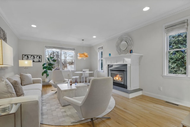 living area with visible vents, baseboards, light wood-style floors, ornamental molding, and a glass covered fireplace