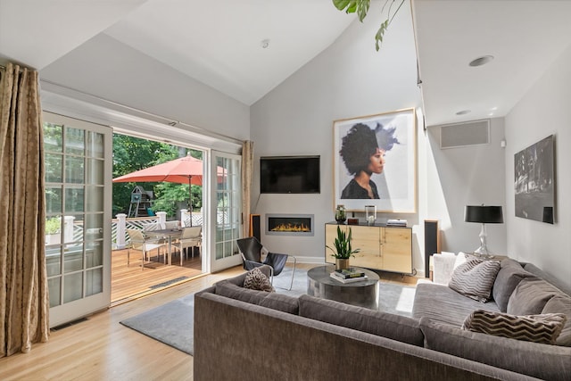 living room with visible vents, high vaulted ceiling, a glass covered fireplace, and light wood-style flooring