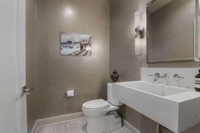 half bath featuring a textured wall, baseboards, a sink, and toilet