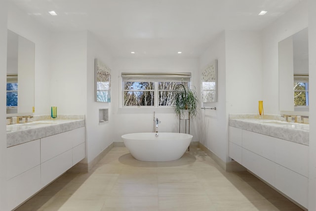 full bathroom featuring baseboards, two vanities, a freestanding bath, a sink, and recessed lighting