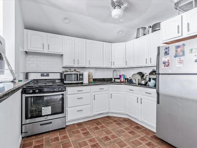 kitchen with sink, stainless steel appliances, dark stone counters, and white cabinets