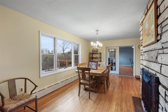 dining area featuring a baseboard radiator, a fireplace, a chandelier, and light hardwood / wood-style flooring