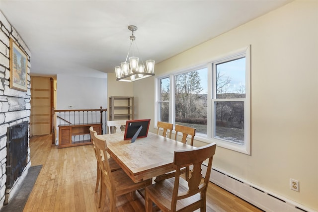 dining room with light hardwood / wood-style flooring, a stone fireplace, a baseboard radiator, and an inviting chandelier