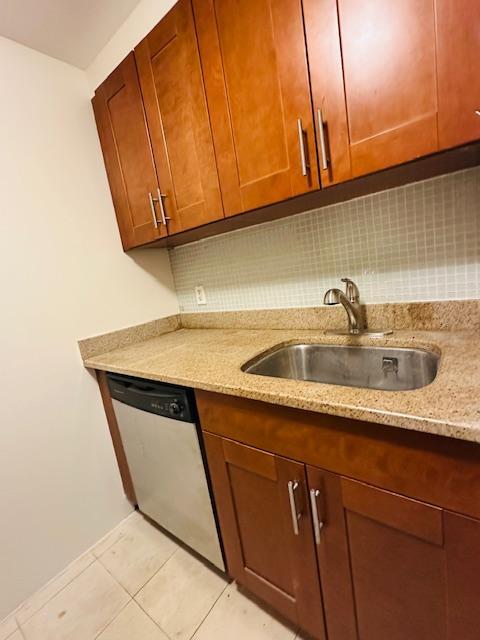 kitchen with sink, tasteful backsplash, light tile patterned floors, dishwasher, and light stone countertops