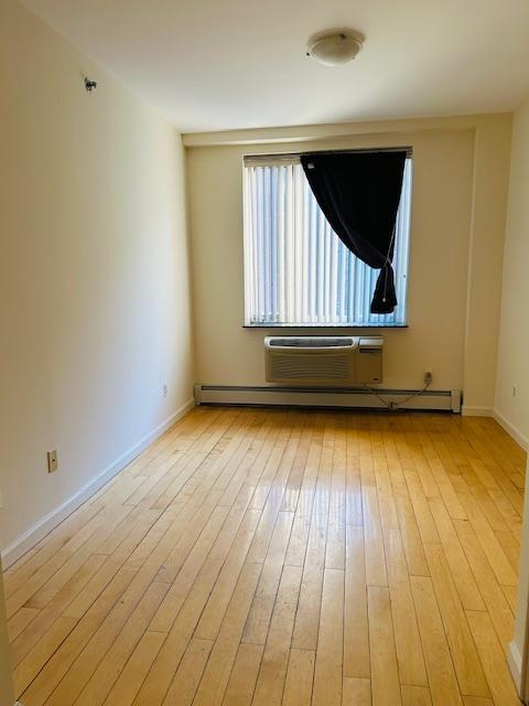 spare room with baseboard heating, a wall unit AC, and light wood-type flooring