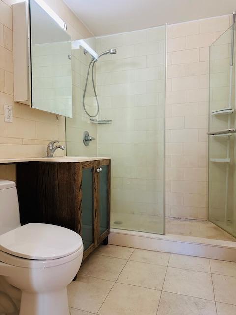 bathroom featuring tiled shower, vanity, toilet, and tile patterned flooring