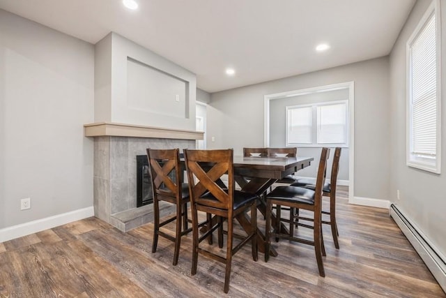 dining room featuring a healthy amount of sunlight, dark hardwood / wood-style flooring, a tile fireplace, and a baseboard heating unit