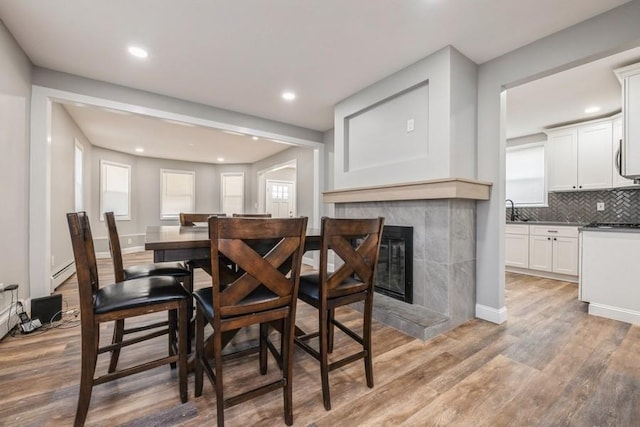 dining area featuring sink, a tiled fireplace, light hardwood / wood-style floors, and a baseboard heating unit