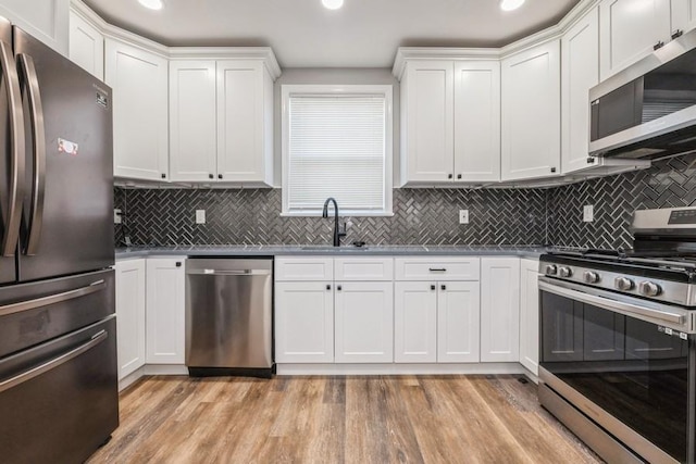 kitchen with sink, backsplash, white cabinets, light hardwood / wood-style floors, and stainless steel appliances