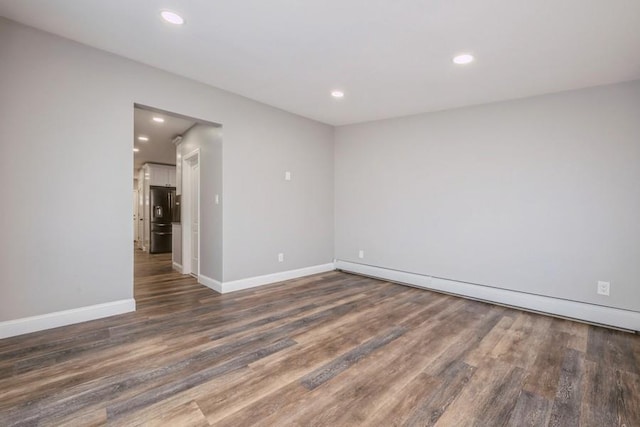 unfurnished room with dark wood-type flooring and a baseboard heating unit