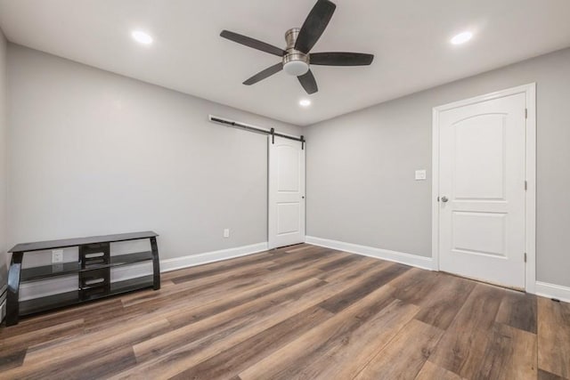 empty room featuring a barn door, dark wood-type flooring, and ceiling fan