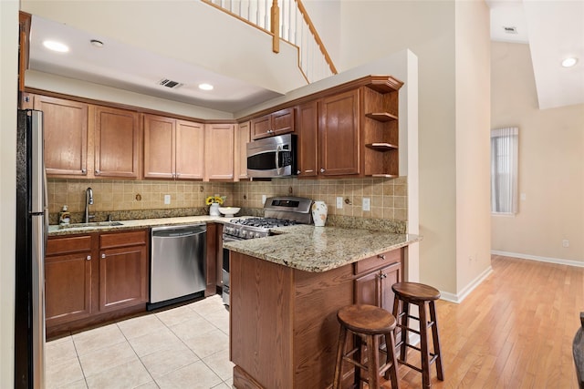 kitchen featuring a kitchen bar, sink, light stone counters, appliances with stainless steel finishes, and kitchen peninsula