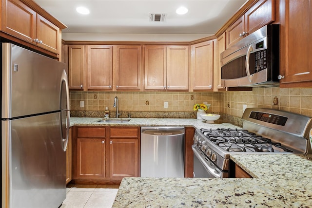 kitchen with sink, light tile patterned floors, appliances with stainless steel finishes, light stone countertops, and backsplash