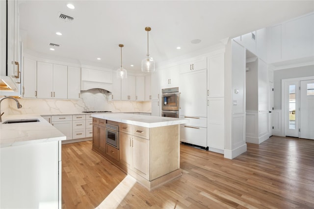 kitchen with pendant lighting, sink, white cabinetry, double oven, and a center island