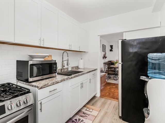 kitchen featuring appliances with stainless steel finishes, sink, white cabinets, light parquet floors, and light stone counters