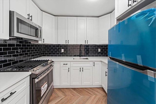 kitchen with white cabinetry, appliances with stainless steel finishes, sink, and light parquet flooring