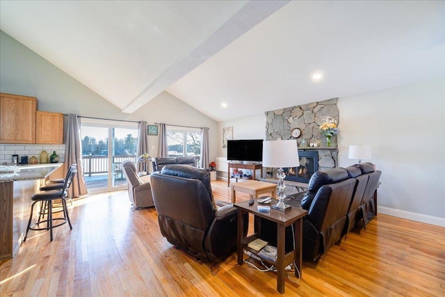 living room with high vaulted ceiling, a stone fireplace, and light hardwood / wood-style floors