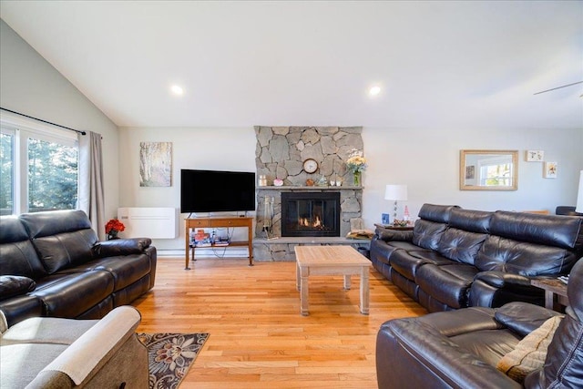 living room featuring vaulted ceiling, a stone fireplace, and light hardwood / wood-style flooring