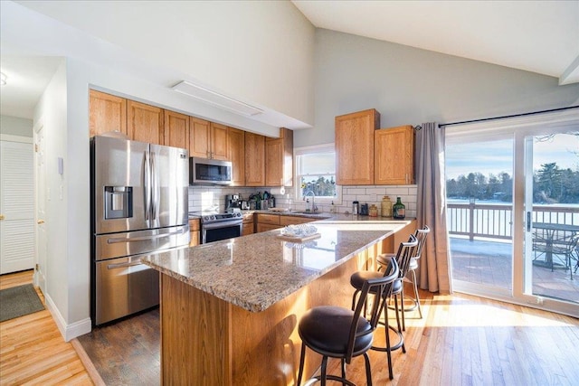 kitchen featuring tasteful backsplash, appliances with stainless steel finishes, a kitchen island, light stone countertops, and hardwood / wood-style floors