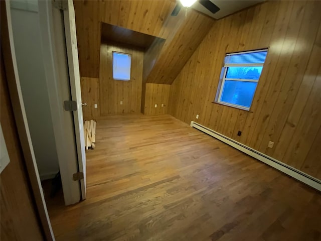 additional living space with lofted ceiling, wood-type flooring, wooden walls, ceiling fan, and a baseboard heating unit