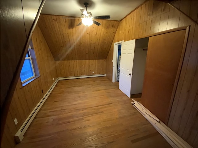 additional living space with a baseboard radiator, lofted ceiling, light hardwood / wood-style flooring, and wood walls