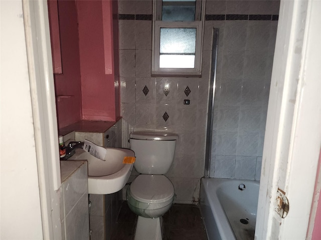 bathroom with tile walls, a bath, sink, and toilet