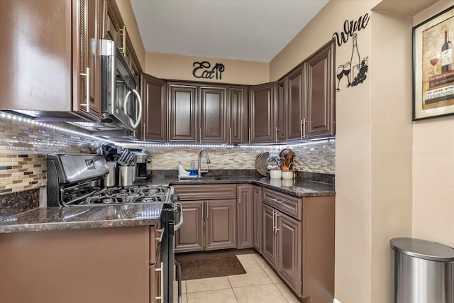 kitchen featuring light tile patterned flooring, sink, stainless steel gas stove, dark stone countertops, and decorative backsplash