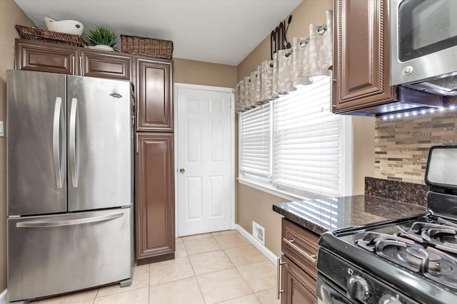 kitchen featuring tasteful backsplash, light tile patterned floors, stainless steel appliances, and dark stone counters