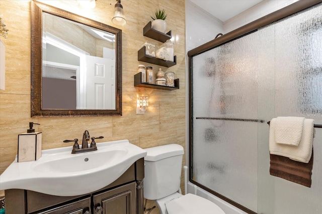 full bathroom with combined bath / shower with glass door, tile walls, backsplash, vanity, and toilet