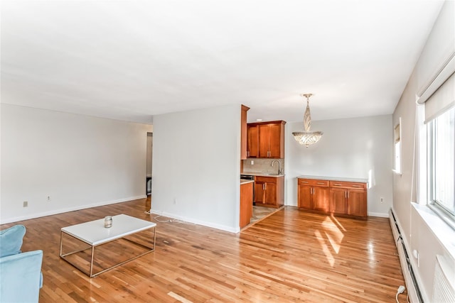 unfurnished living room featuring a baseboard heating unit, sink, a notable chandelier, and light wood-type flooring