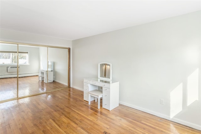 unfurnished bedroom featuring a closet, a baseboard heating unit, a wall mounted air conditioner, and light wood-type flooring